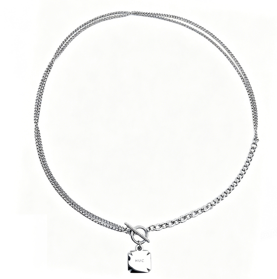 Silver-tone double curb-chain necklace with bar-and-ring toggle clasp and a small engraved square tag, on a white background.